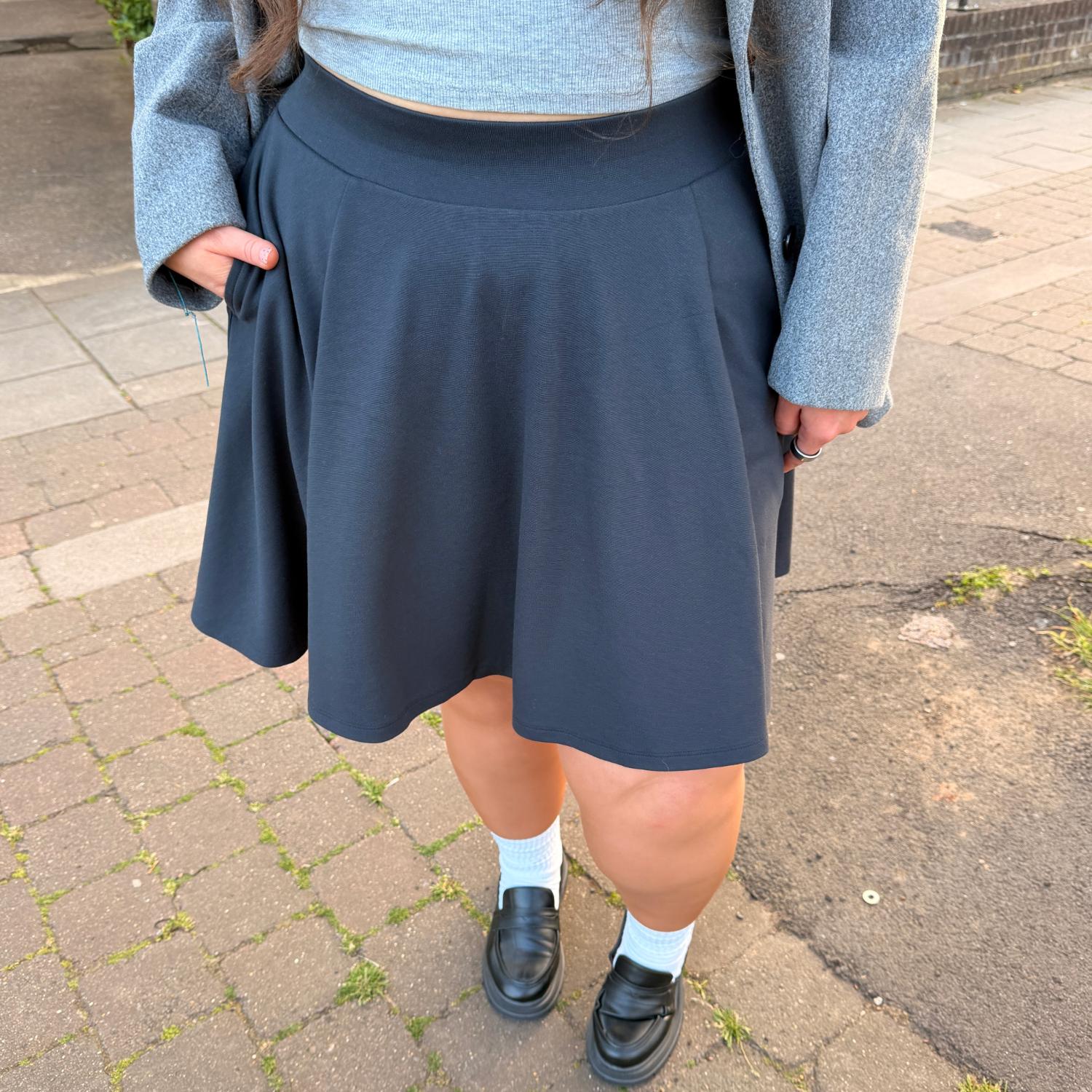 Person wearing a charcoal skirt with a gray sweater and black shoes on a sidewalk.