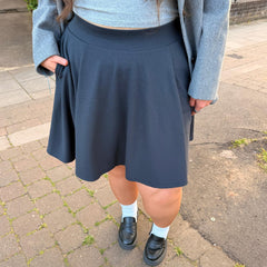 Person wearing a charcoal skirt with a gray sweater and black shoes on a sidewalk.
