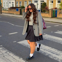 Woman walking on a street wearing a gray coat and charcoal skirt.